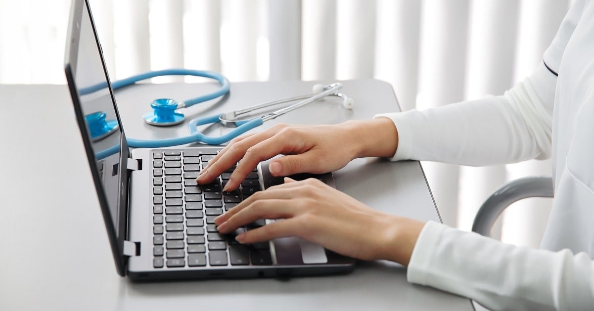 A healthcare professional typing on a laptop