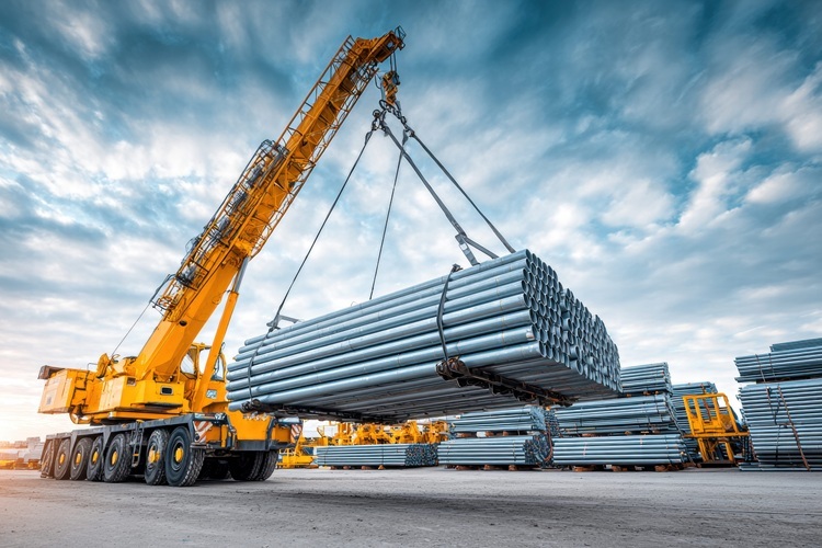 Crane lifting metal pipes in an industrial area