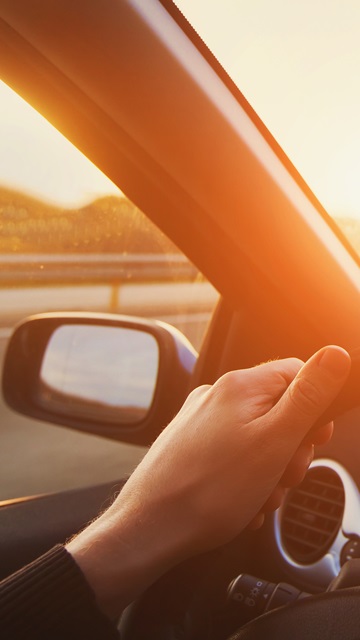 Man holding a car's steering wheel driving on the road